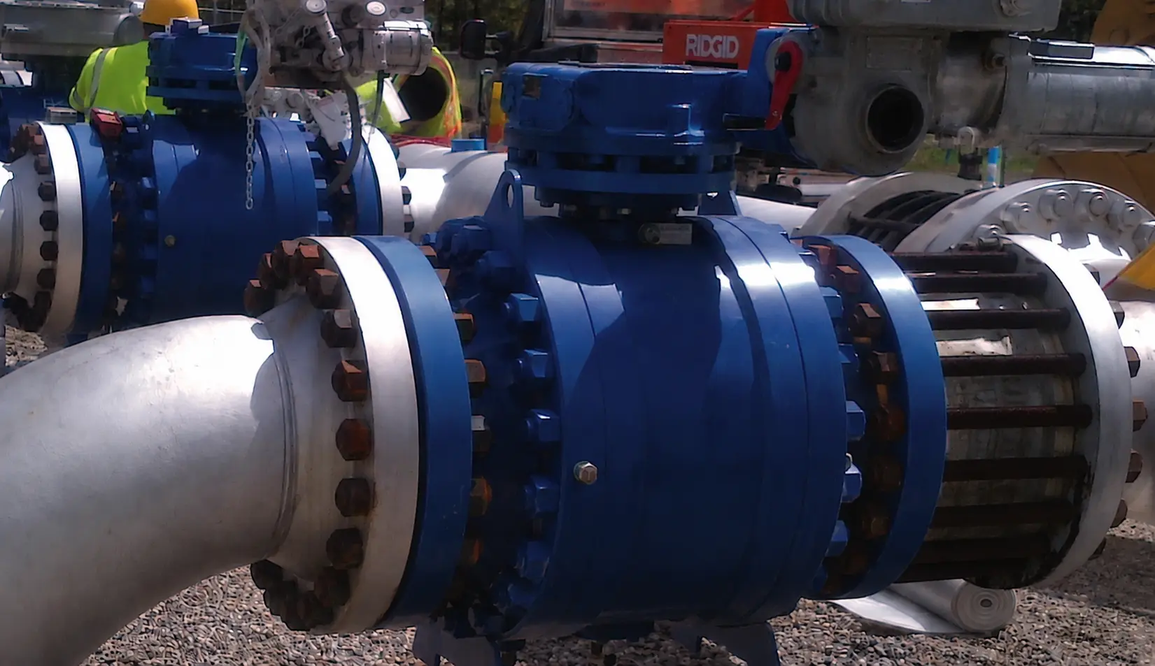 Flanged industrial ball valve with manual lever handle installed on a process pipeline at a refinery.